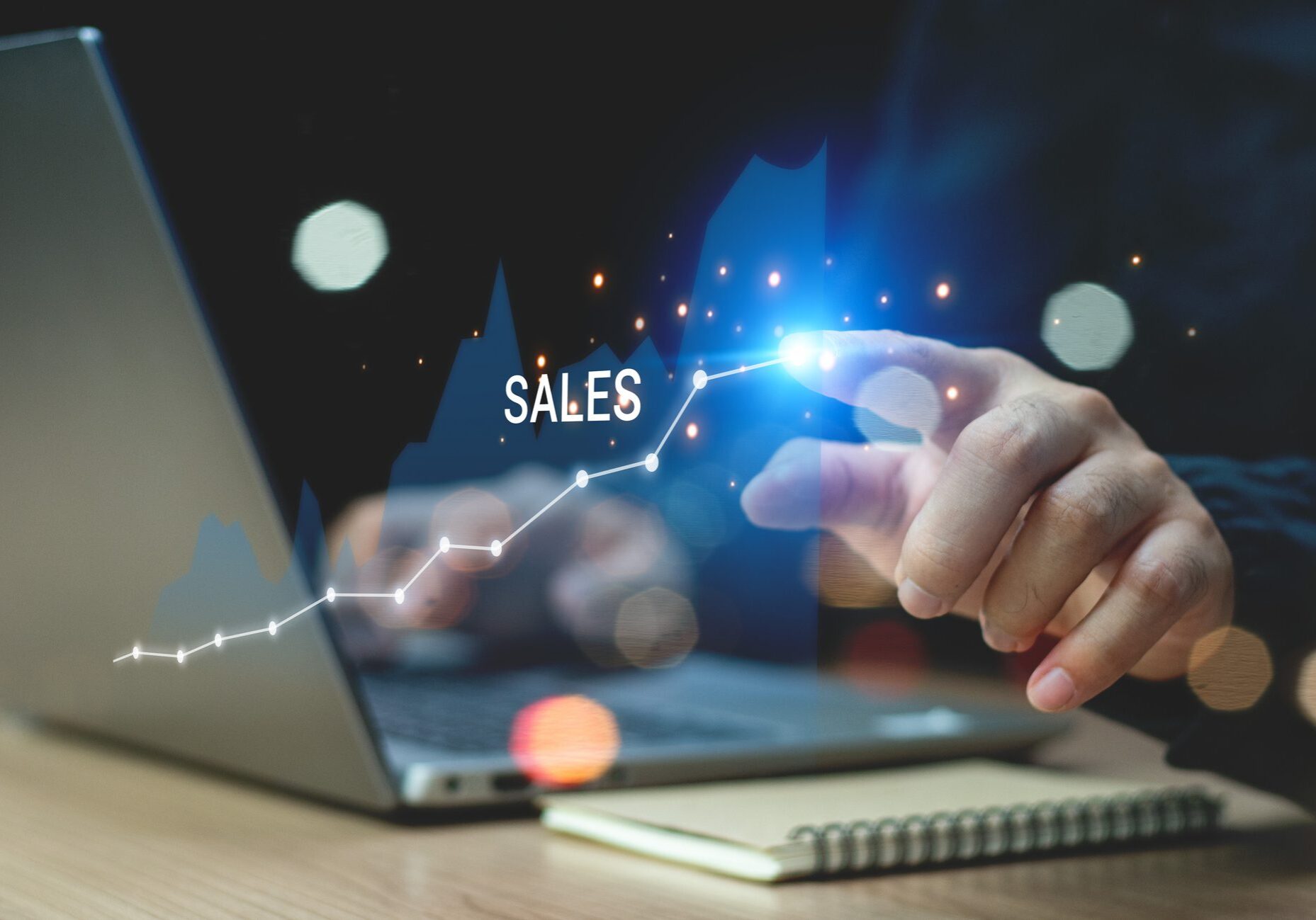 Finger touching sales growth graph on laptop.